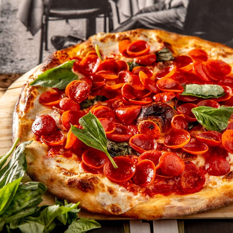 A Brooklyn Born pepperoni pizza with fresh basil leaves on a wooden board.